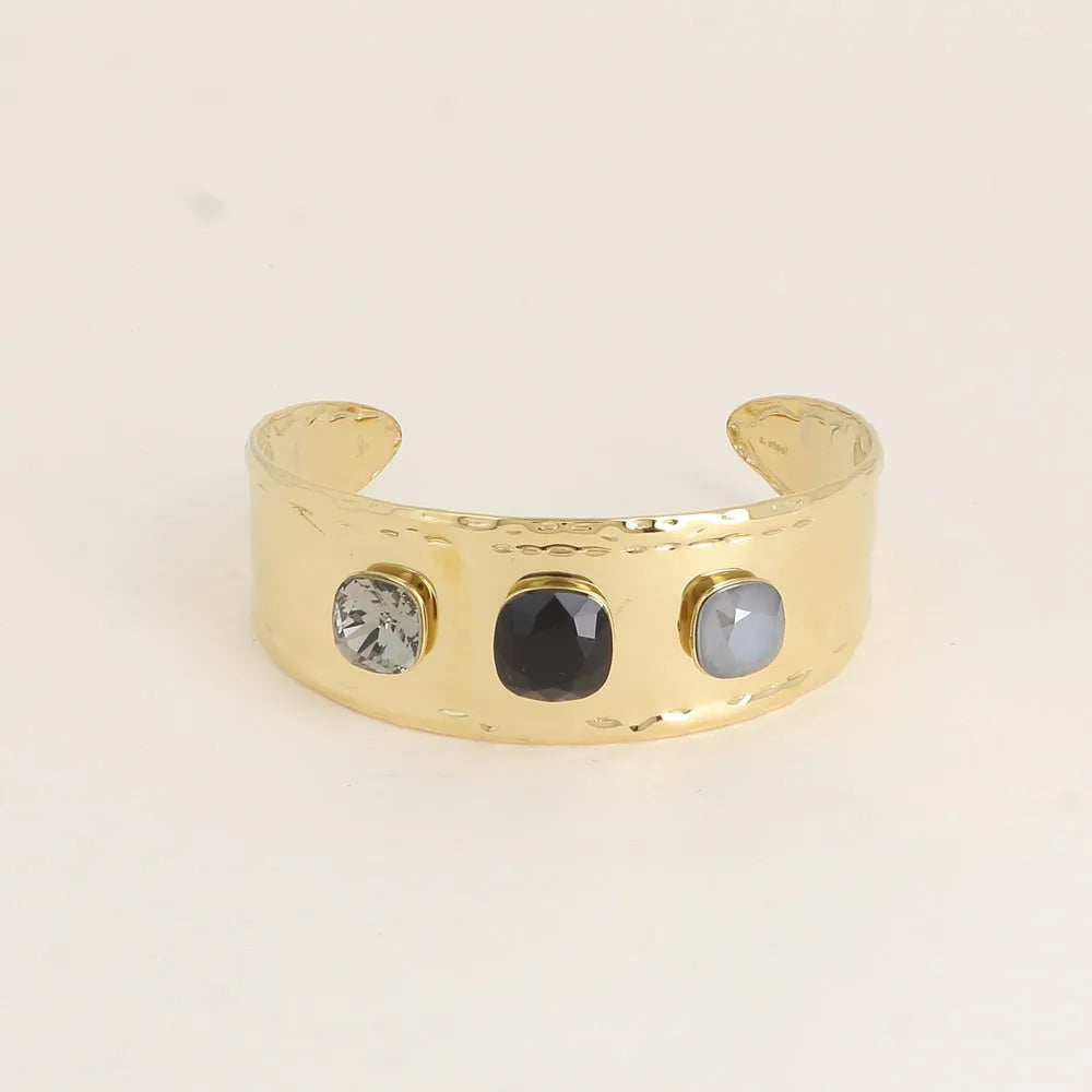 Kullanvärinen leveä ja säädettävä Bohm Paris -rannekoru, jossa on kolme mustan ja harmaan sävyistä neliönmuotoista Swarovski-kristallia.