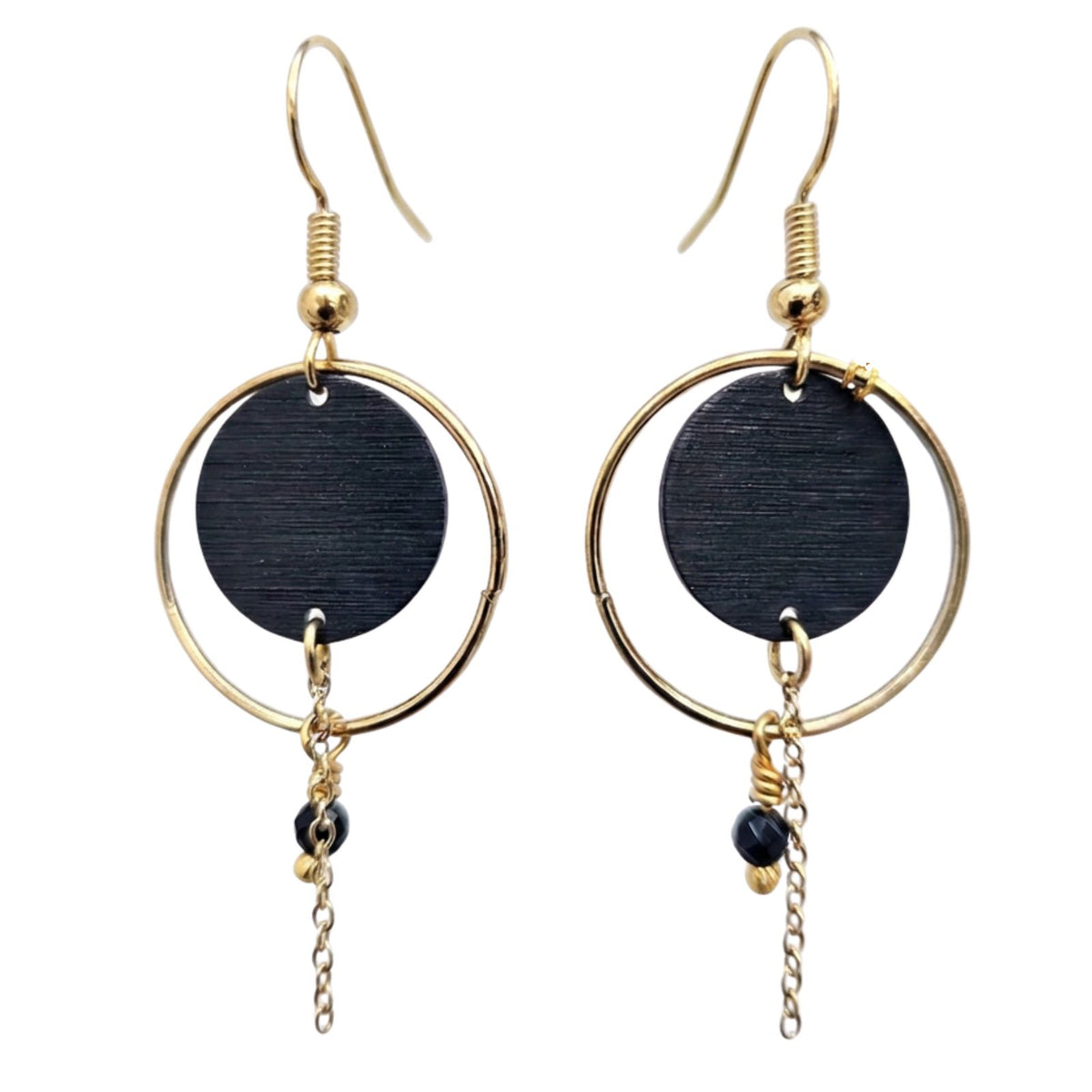 Bijoux Enora Noir Soleil -riippuvat korvakorut, joissa on kullanvärinen ohut rengas, musta puinen tai kuvioitu pyöreä laatta ja siro roikkuva ketju.