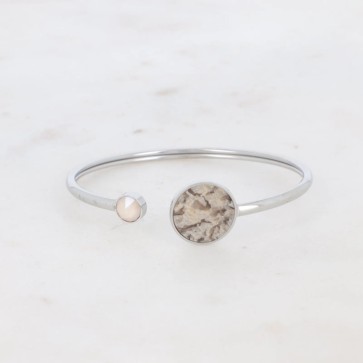 Jäykkä hopeanvärinen kirurginteräksinen avorannekoru, jossa on pyöreä maisemajaspis-luonnonkivi ja toisessa päässä pieni nude-sävyinen Swarovski-kristalli.