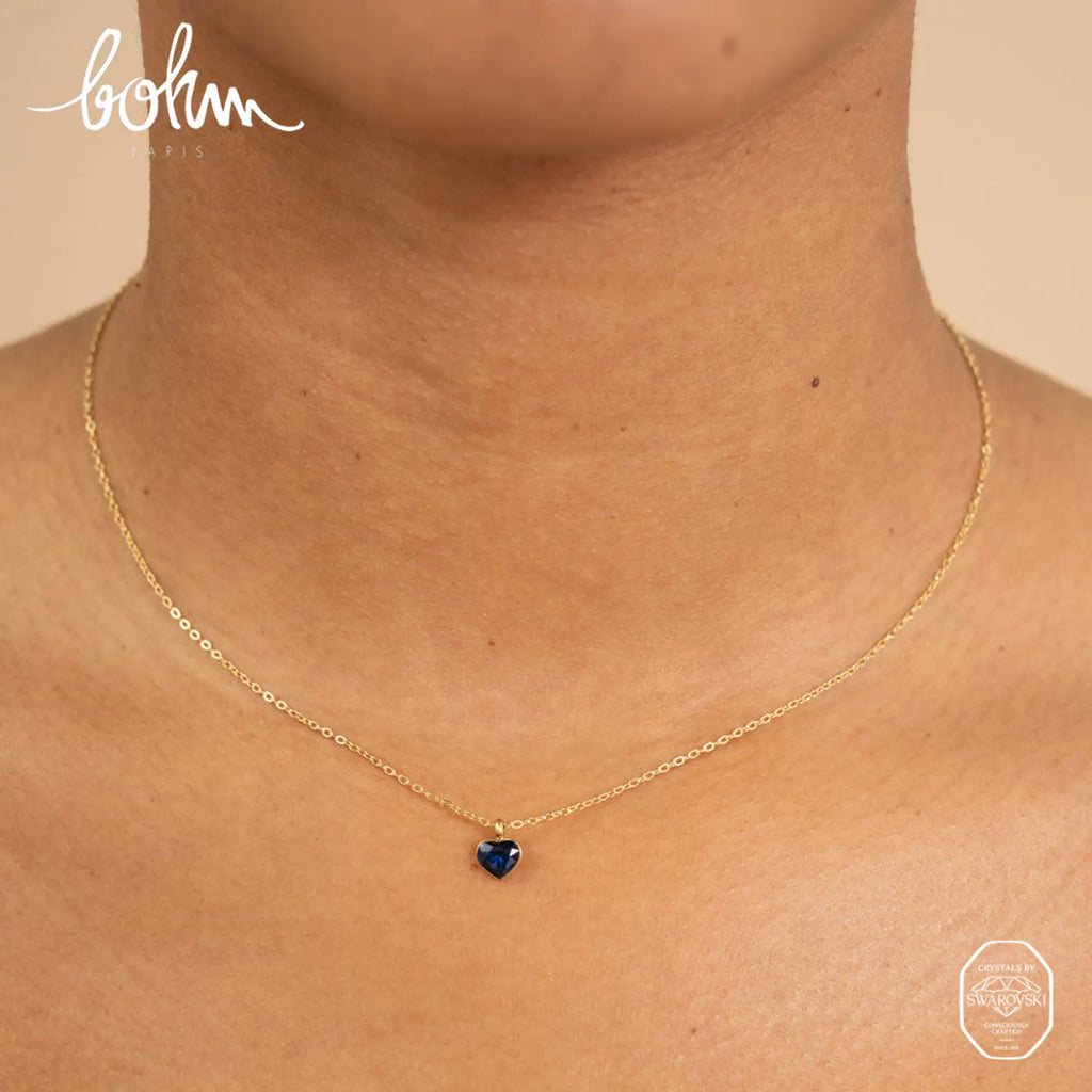 Siro kullanvärinen Bohm Paris Coeur sydänkaulakoru kaulassa osoittamassa safiirinsinisen Swarovski-kristalliriipuksen todellisen koon ja istuvuuden.
