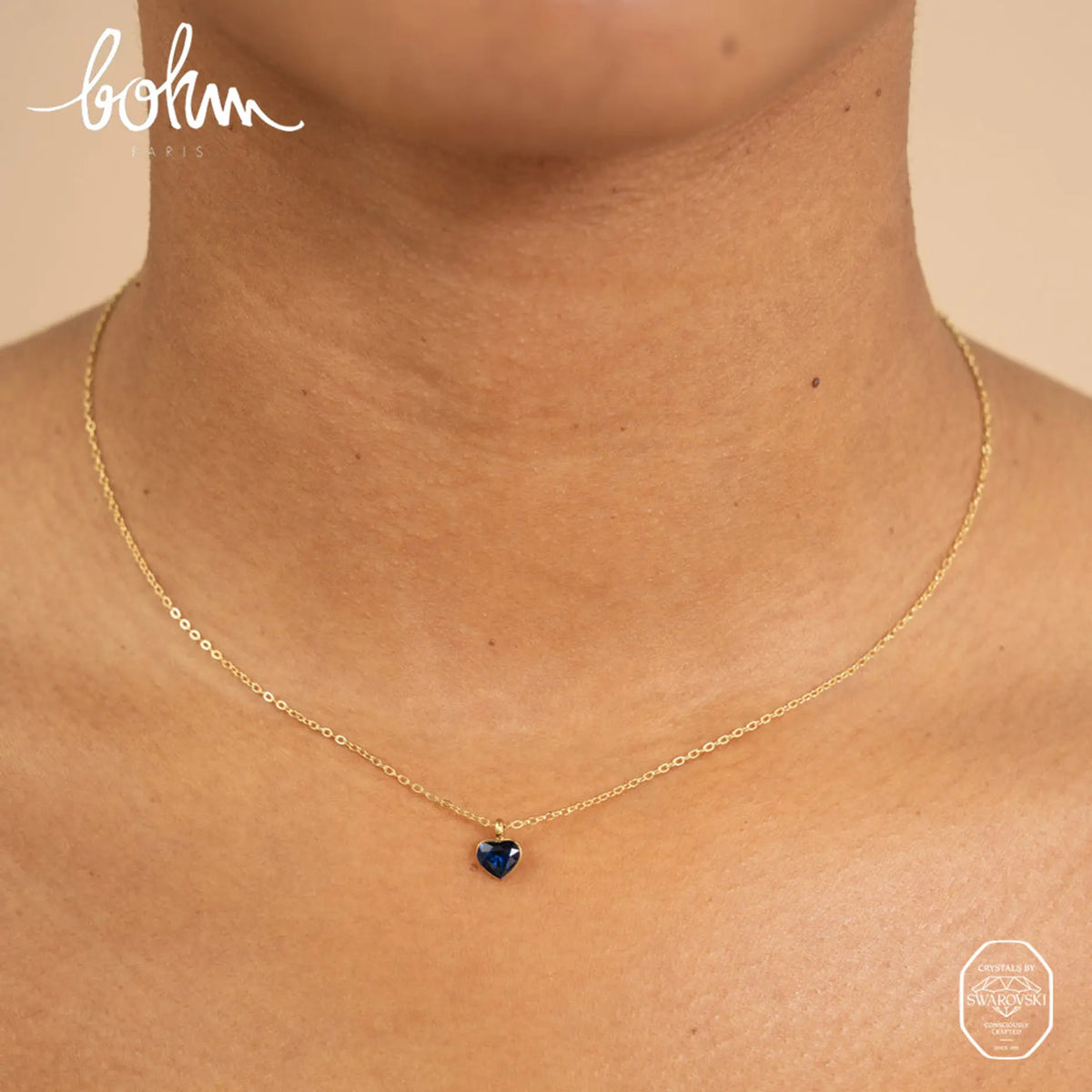 Siro kullanvärinen Bohm Paris Coeur sydänkaulakoru kaulassa osoittamassa safiirinsinisen Swarovski-kristalliriipuksen todellisen koon ja istuvuuden.
