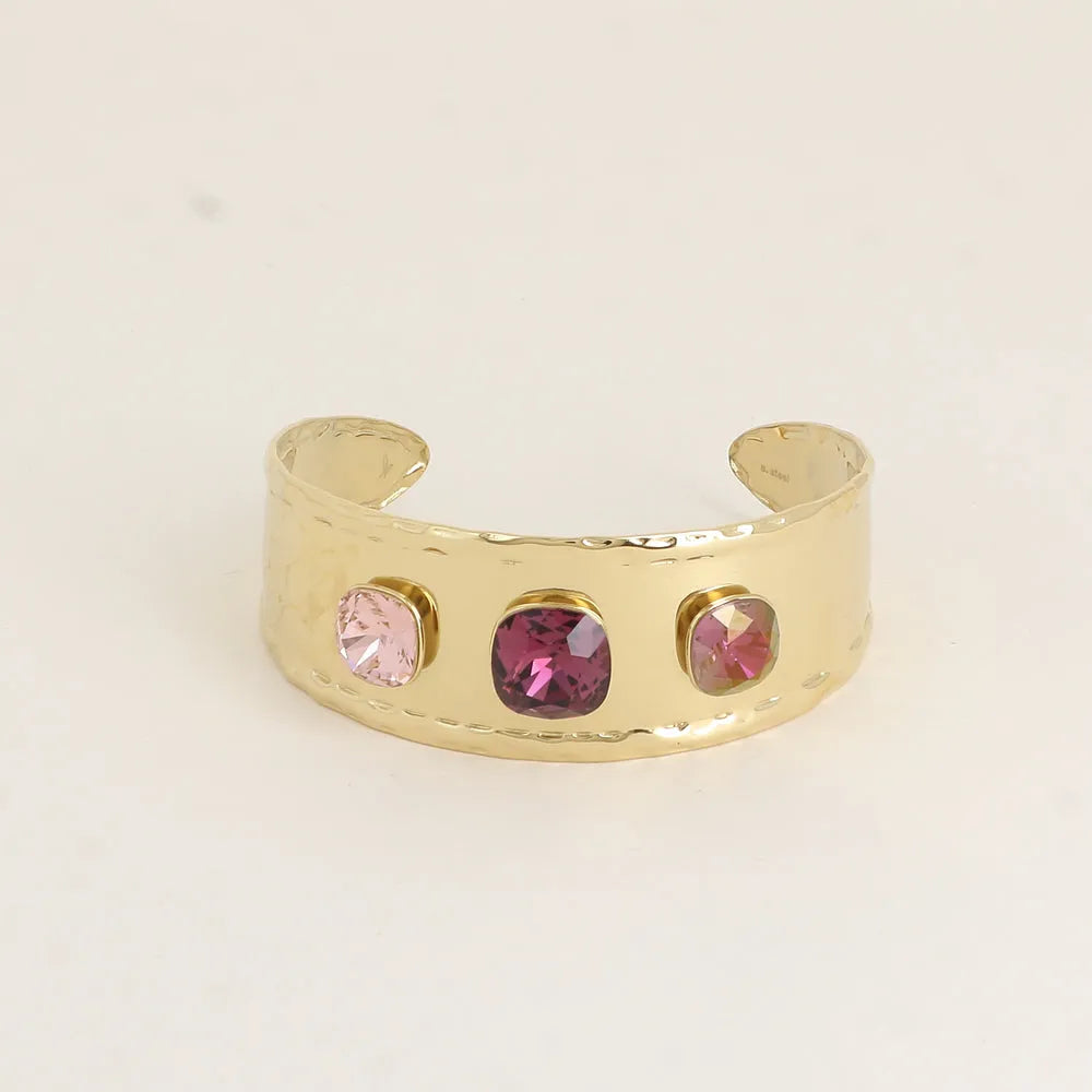 Kullanvärinen leveä ja säädettävä Bohm Paris -rannekoru, jossa on kolme vaaleanpunaisen ja violetin sävyistä neliönmuotoista Swarovski-kristallia.