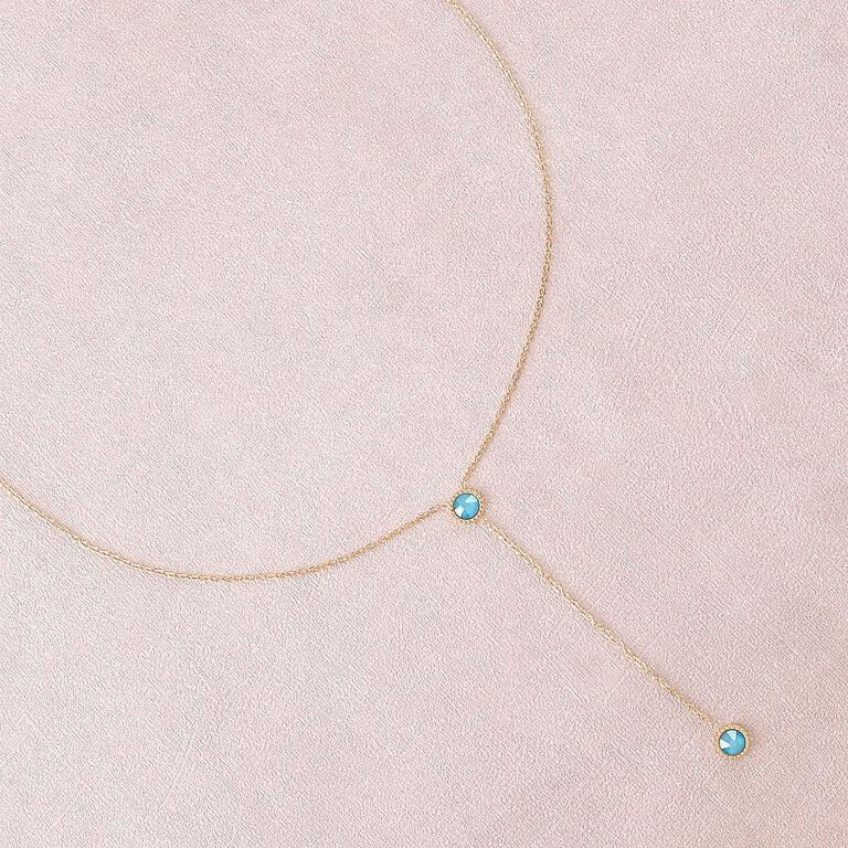 Siro kullanvärinen Y-kaulakoru, jossa on kaksi pientä pyöreää ja kirkkaan turkoosia Swarovski-kristallia vaaleanpunaisella taustalla.