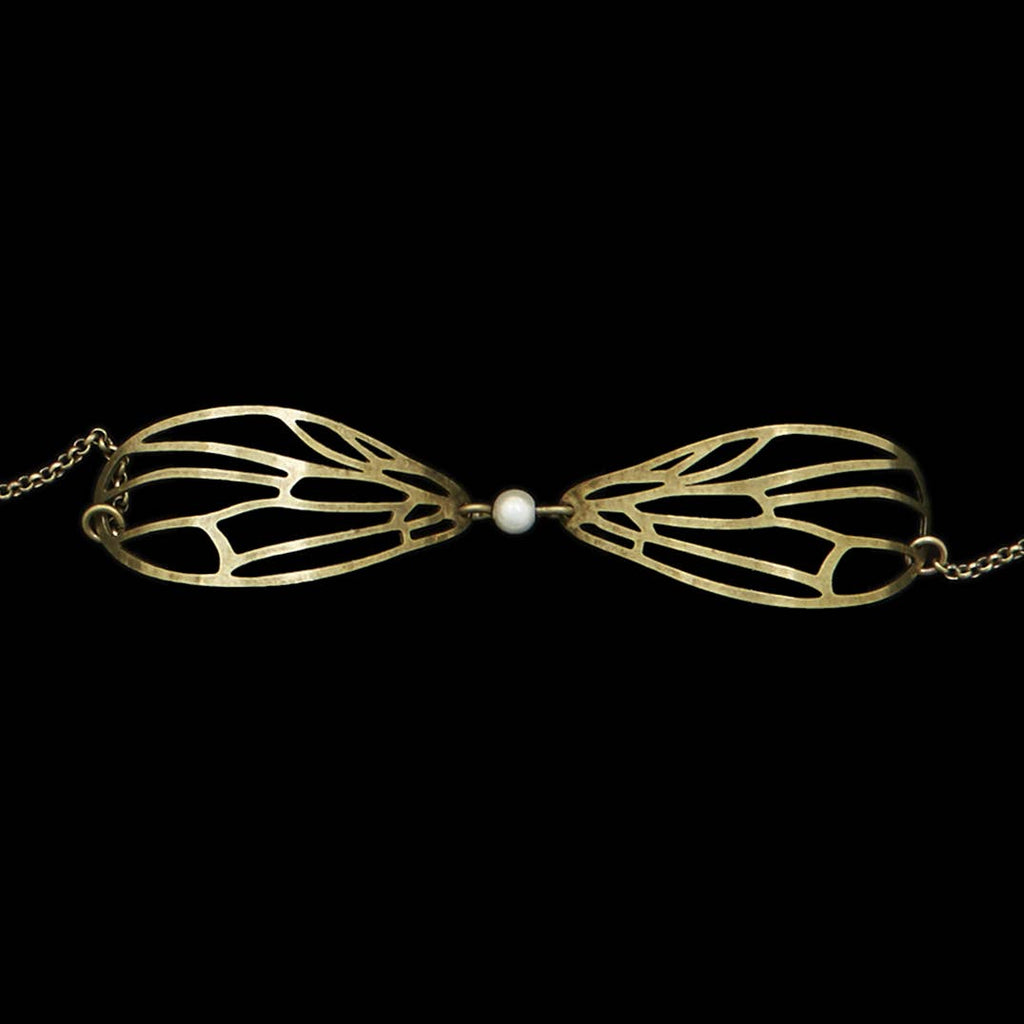 Lähikuva Amélie Blaise Dragonfly White Pearl -rannekorusta, jossa on pronssiset sudenkorennon siivet ja keskellä valkoinen helmi sirossa ketjussa.